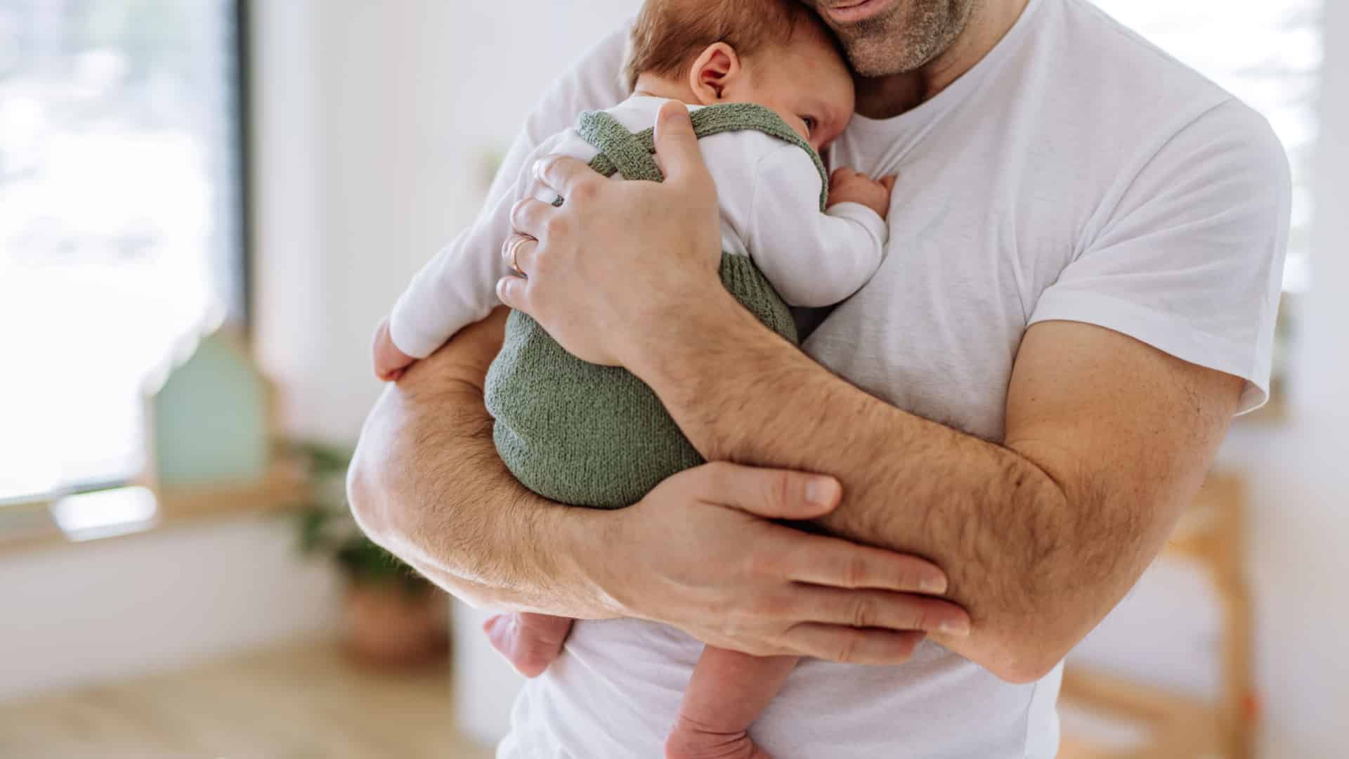 Primul plan al unui tata care isi tine copilul aproape de piept.